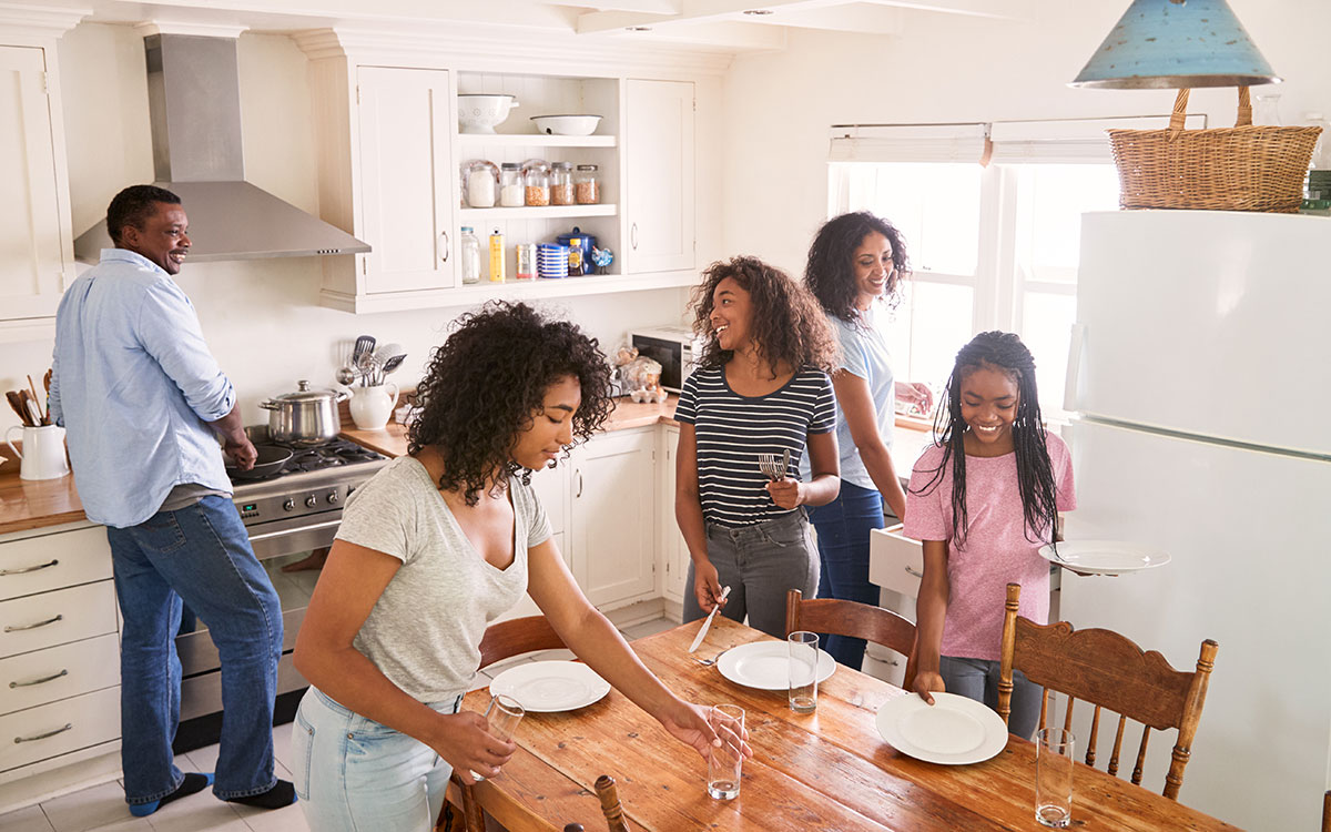 African American family of five in their daily morning routine, with three teen girls standing in the kitchen.