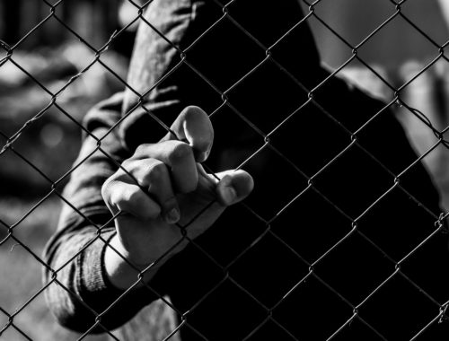 Image of antisocial, withdrawn teen, holding onto a fence.