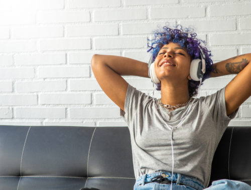 Young teen with blue hair listening to music and smiling.