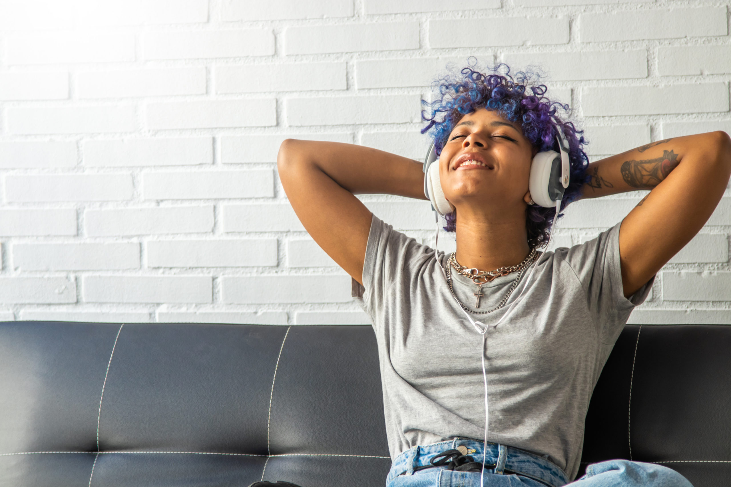 Young teen with blue hair listening to music and smiling.