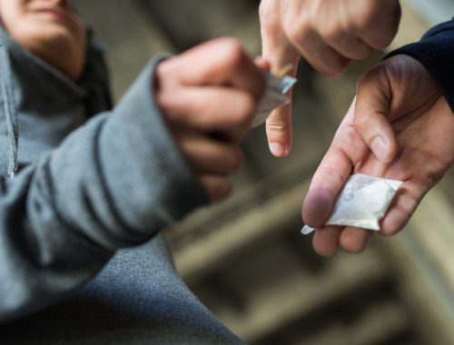 Teens passing each other drugs in front of a brick wall.