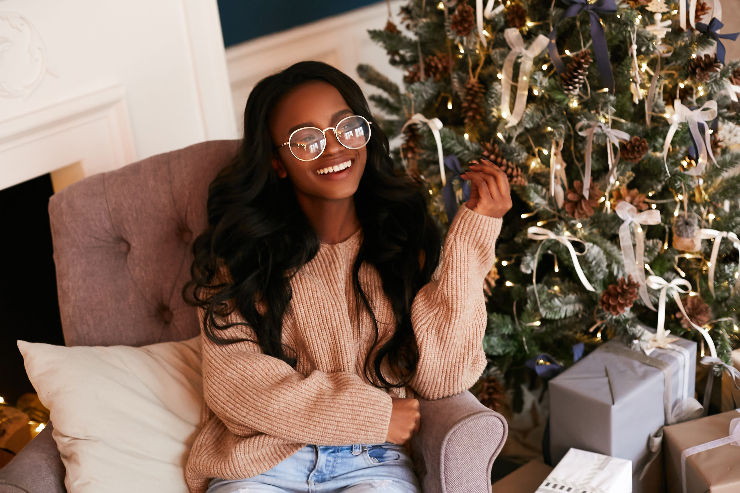 Smiling teenage girl sitting next to a christmas tree.